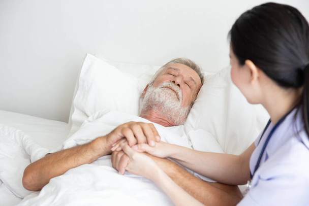 Η νοσοκόμα φροντίζει τους ηλικιωμένους που κοιμούνται στο κρεβάτι. - Φωτογραφία, εικόνα