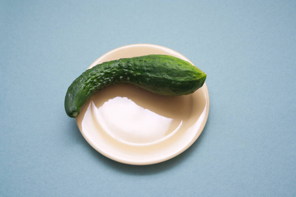 Natural cucumber of an unusual shape on a yellow plate on a blue background. The idea of a healthy natural diet without gmo - Foto, afbeelding