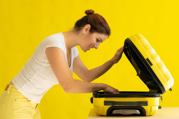 Caucasian woman going on vacation and packing suitcase on yellow background - Photo, image