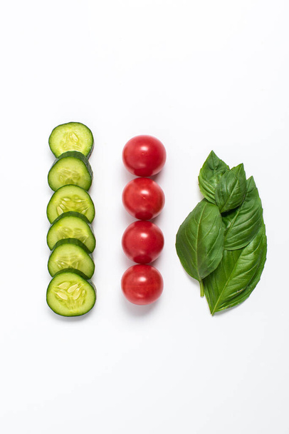 Creative mockup of tomato slices, cucumber and basil leaves. Flat lay, top view. Food concept. Vegetables isolated on a white background. - Fotoğraf, Görsel