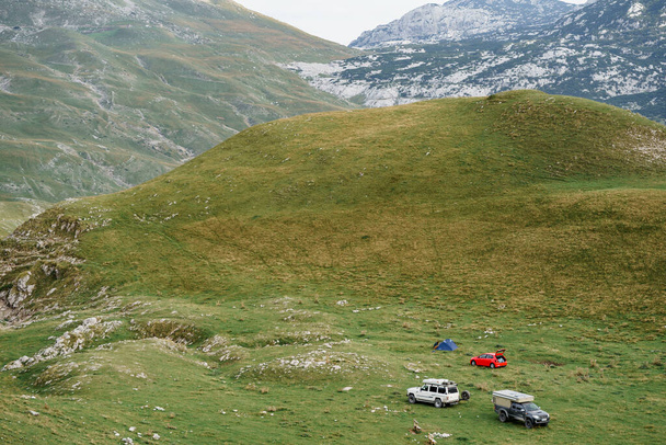 Οι τουρίστες έστησαν ένα στρατόπεδο αυτοκινήτων στα βουνά, στο πράσινο γρασίδι. Μαυροβούνιο, Εθνικό Πάρκο Durmitor. - Φωτογραφία, εικόνα