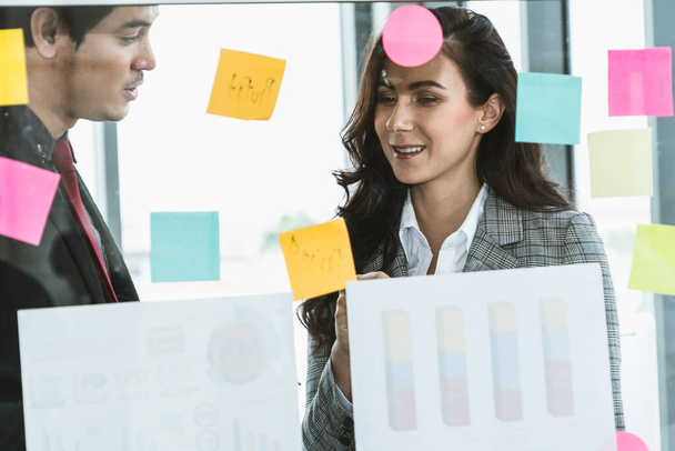 Business people work on project planning board in office and having conversation with coworker friend to analyze project development . They use sticky notes posted on glass wall to make it organized . - Foto, imagen