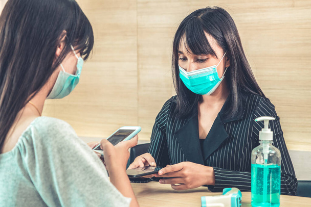 Receptionist en gast dragen gezichtsmasker aan de receptie tijdens een gesprek in kantoor of ziekenhuis. Covid 19 en coronavirus bescherming en beschermende beleid concept . - Foto, afbeelding