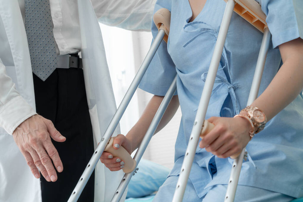 医者は病院で松葉杖の患者の世話をする。理学療法士と足の怪我の回復コンセプト. - 写真・画像