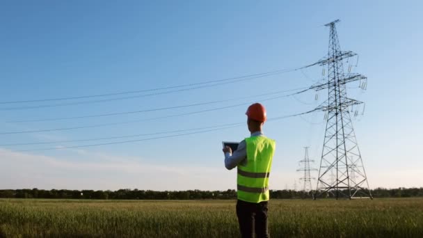 Two power engineers meet near power lines and discuss reconstruction of high-voltage lines on a paper plan. - Footage, Video