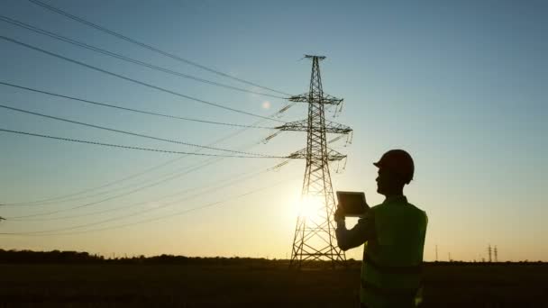 De power engineer voert een power line state inspectie met behulp van een tablet, zonsondergang achtergrond. - Video