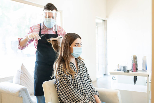 Männlicher Friseur schneidet bei Coronavirus-Ausbruch Haare einer Kundin im Salon - Foto, Bild