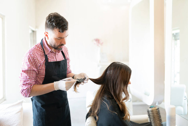 Male hairdresser applying dye on hair of young woman at beauty studio - Photo, Image