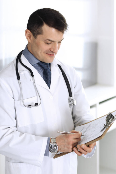 Doctor man using clipboard for filling up medication history records. Perfect medical service in clinic. Physician at work in hospital. Medicine and healthcare concepts - Fotó, kép