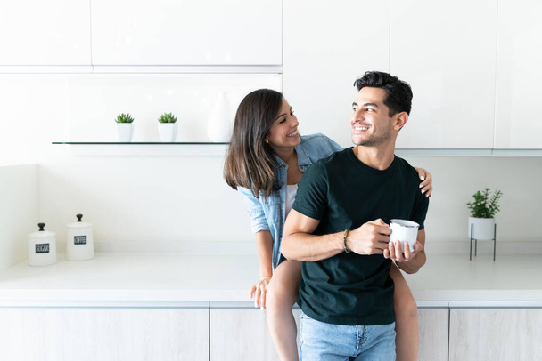 Sorridente donna latina guardando il fidanzato mentre seduto sul bancone della cucina - Foto, immagini