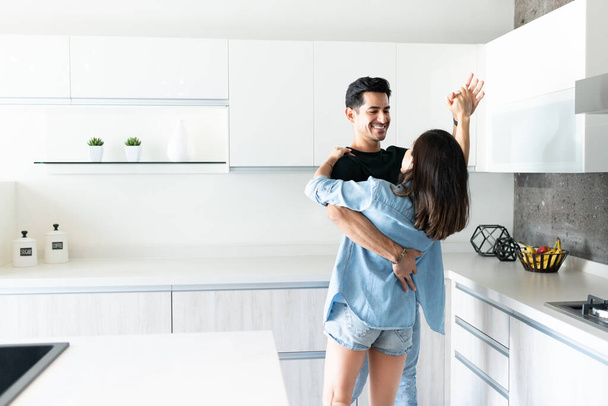 Hispanic young couple dancing in kitchen at home - Φωτογραφία, εικόνα