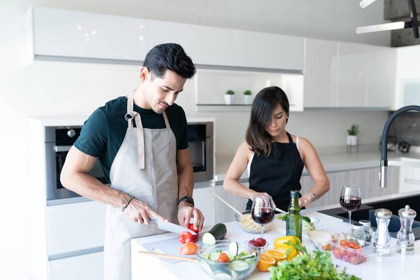 Spanisches junges Paar hackt Gemüse, während es zu Hause Pasta zubereitet - Foto, Bild