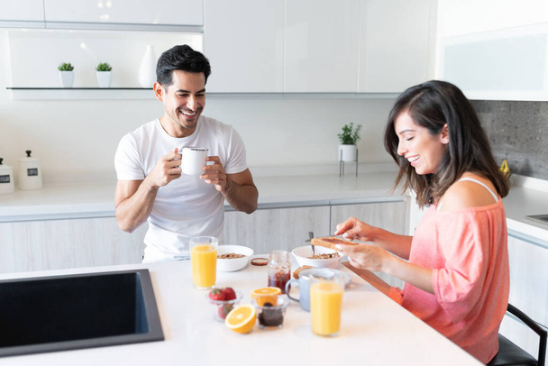 Feliz namorado bebendo café enquanto namorada aplicando geléia no pão durante o café da manhã
 - Foto, Imagem
