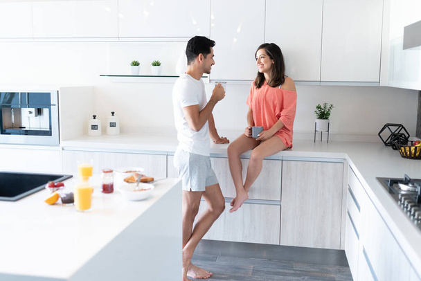 Hispanic young couple talking while drinking coffee in morning at home - Photo, Image
