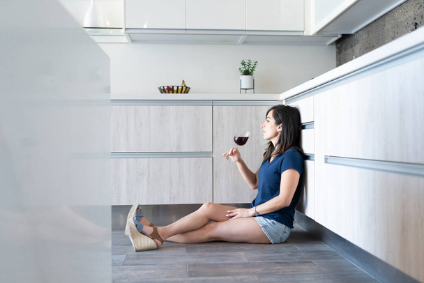 Seitenansicht einer jungen Frau, die in der Küche Wein trinkt - Foto, Bild