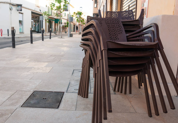Sillas de plástico marrón apiladas junto a mesas al aire libre. Restaurante cerrado por Coronavirus - Foto, imagen