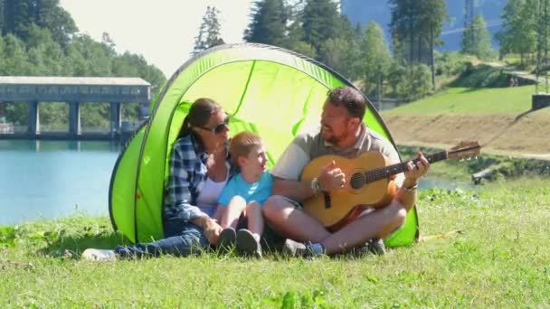 Wesoły rodzinny kemping nad rzeką, gra na gitarze i śpiewa razem piosenkę w namiocie. - Materiał filmowy, wideo