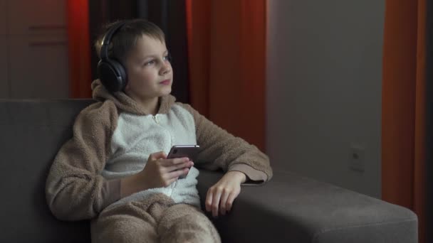 Der Mann mit den Kopfhörern und dem Smartphone in der Hand sitzt auf der Couch und hört Musik. Quarantäne 2020 - Filmmaterial, Video