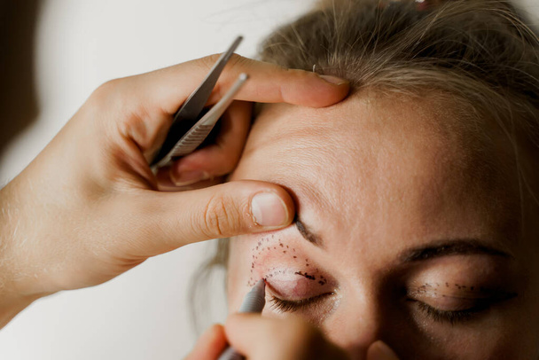 Primo piano del markup della blefaroplastica sul viso prima dell'intervento di chirurgia plastica per modificare la regione oculare del viso in clinica medica. 2 medici fanno operazioni cosmetiche di plastica - Foto, immagini