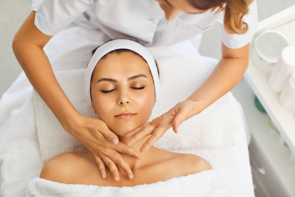Beautician makes a facial massage to a woman in a spa salon. Woman receiving face protection treatment procedures - Foto, imagen