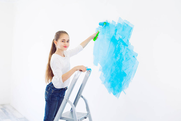 Repair in the apartment. Happy child girl paints the wall with blue paint, - Foto, imagen