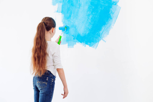 Repair in the apartment. Happy child girl paints the wall with blue paint, - Photo, image