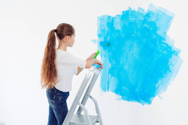 Repair in the apartment. Happy child girl paints the wall with blue paint, - Photo, image