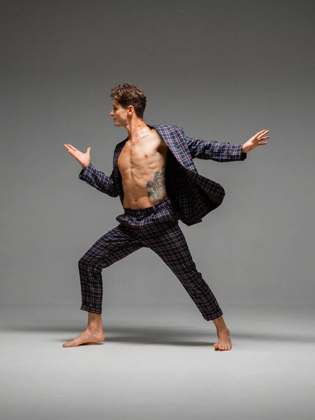 Handsome young guy breakdancer dancing expressive dance in suit with naked torso isolated on gray background - Foto, Bild
