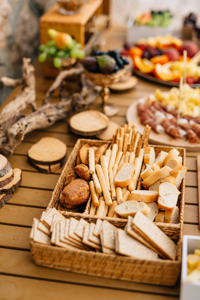 Wicker bread and cereal tray with sliced loaf, bread sticks and cookies on a wooden holiday table. - Photo, Image