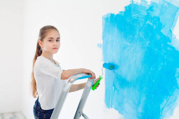 Repair in the apartment. Happy child girl paints the wall with blue paint, - Fotoğraf, Görsel