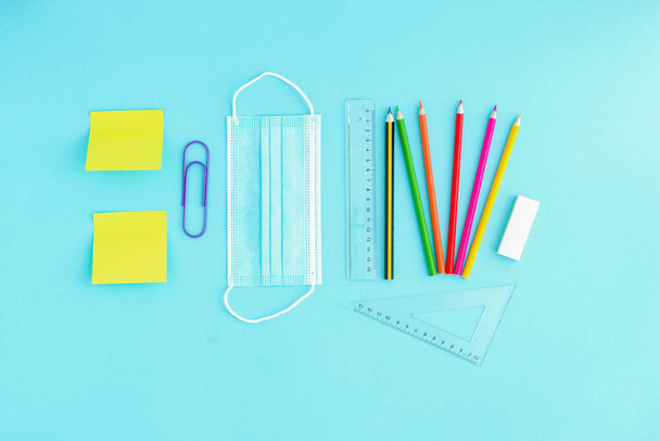 Lékařský štít a barevné tužky, sponky a samolepky na světle modrém pozadí. Zpátky do školy po pandemii, kancelářské práce během karantény - Fotografie, Obrázek