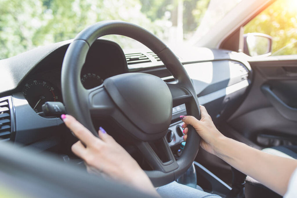 Blisko kobieta ręce trzymając kierownicę podczas siedzenia w nowoczesnym wnętrzu pojazdu. Dziewczyna jazdy samochodem na koncepcji ulicy - Zdjęcie, obraz