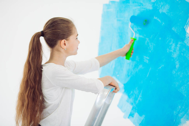 Repair in the apartment. Happy child girl paints the wall with blue paint, - Foto, imagen