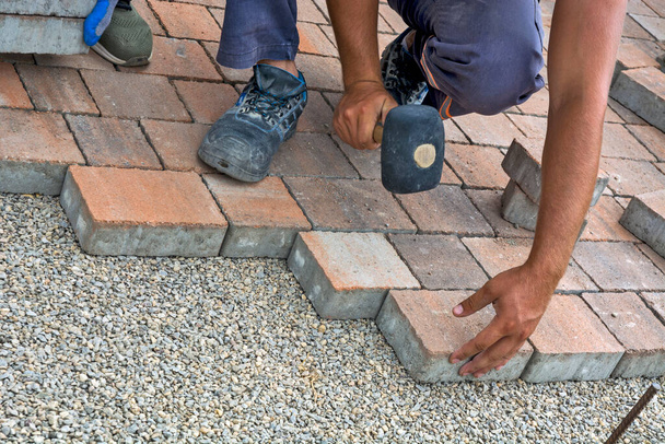 Maestro poner e instalar ladrillos de piso en una superficie pública. La base es de piedra pequeña y se ajustan a piezas decorativas de hormigón de ladrillo. - Foto, imagen