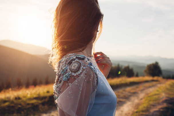 Beautiful bride wearing blue wedding dress in mountains at sunset. Young woman enjoys summer landscape. Close up of fashionable decor - Photo, Image
