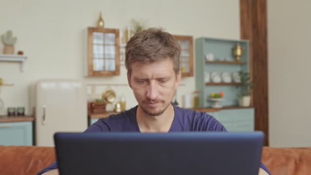 Uomo caucasico trascorrere del tempo libero sul divano e utilizzando il computer portatile a casa moderna. Concetto di giovani che godono di dispositivi mobili - Filmati, video