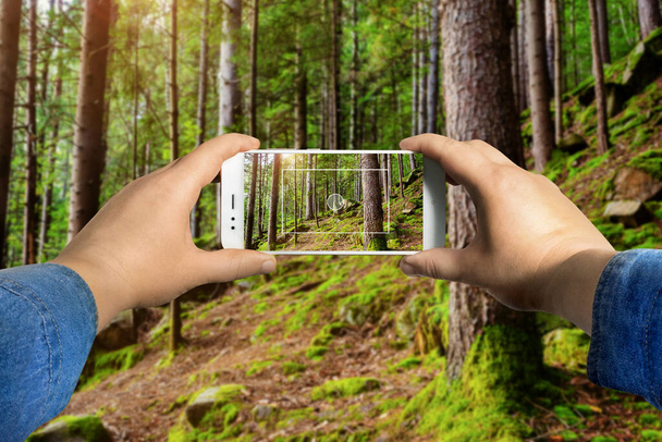 Ego-View-Foto einer männlichen Hand in Jeanshemd mit Smartphone und Foto im Wald. - Foto, Bild