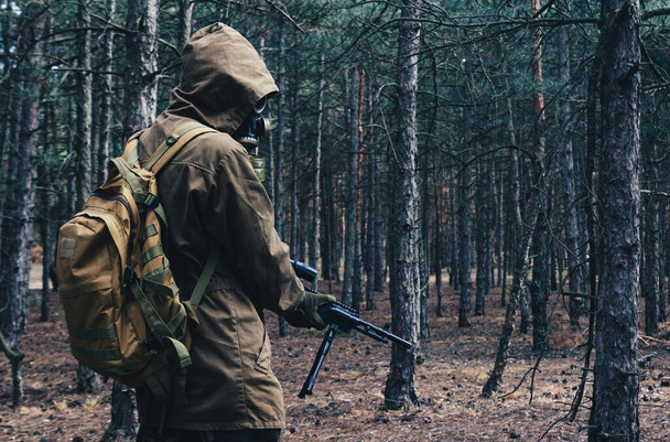 Φωτογραφία ενός στρατιώτη που παρακολουθεί πυρηνικά και ποζάρει με σοβιετική μάσκα αερίου, σακίδιο πλάτης με τουφέκι στο δάσος πίσω όψη. - Φωτογραφία, εικόνα