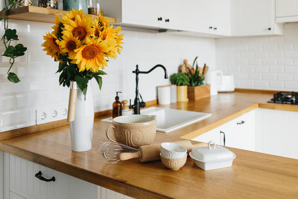Gerechten en keukengerei op keukentafel, klaar om te koken. witte eenvoudige moderne keuken in Scandinavische stijl, keuken details, houten tafel, zonnebloemen boeket in vaas op de tafel - Foto, afbeelding