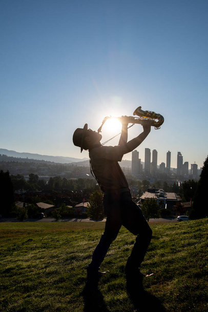 Силуэт человека, играющего на альт-саксофоне на холме, когда восходит солнце. Ванкувер - Фото, изображение