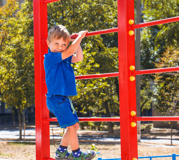 Kleiner blonder Junge auf rotem Kinder-Sportklettergerüst - Foto, Bild