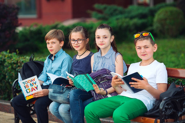 Happy Schoolmates Portrait. Schoolmates seating with books in a wooden bench in a city park and studying on sunny day. - Foto, afbeelding