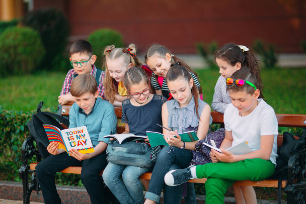 Happy Schoolmates Portret. Schoolvrienden zitten met boeken in een houten bank in een stadspark en studeren op zonnige dag. - Foto, afbeelding
