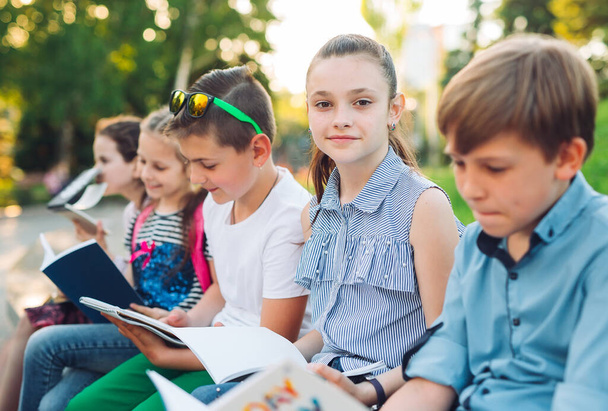 Happy Schoolmates Portrait. Colegas de escola sentadas com livros em um banco de madeira em um parque da cidade e estudando no dia ensolarado
. - Foto, Imagem