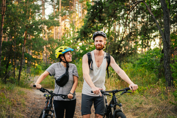 Πανέμορφο ζευγάρι που κάνει ποδήλατο στο δάσος του πάρκου. Ρομαντικό ταξίδι με ποδήλατα. Ενεργό Σαββατοκύριακο. Αθλητικά ζευγάρια. Άνδρες και γυναίκες ποδηλάτες. Οικολογική μεταφορά. uple με ποδήλατα βουνού στο μονοπάτι. - Φωτογραφία, εικόνα