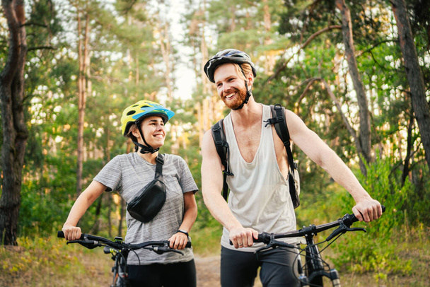 公園の森の中で自転車に乗って豪華なカップル。自転車でロマンチックな旅。週末だ。スポーツカップル。男と女の自転車。環境に優しい交通機関。山道にマウンテンバイクがある人は. - 写真・画像