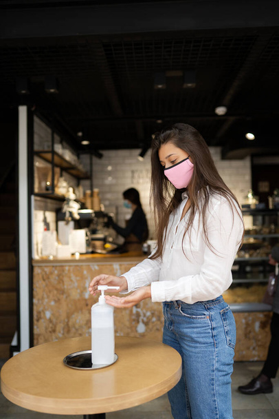 Γυναίκα που χρησιμοποιεί τζελ απολυμαντικό καθαρίζει τα χέρια του ιού coronavirus στο καφέ. - Φωτογραφία, εικόνα