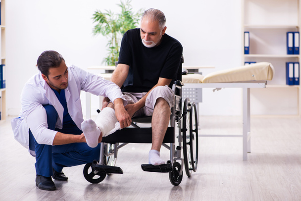 Homem velho ferido visitando jovem médico traumatologista masculino
 - Foto, Imagem