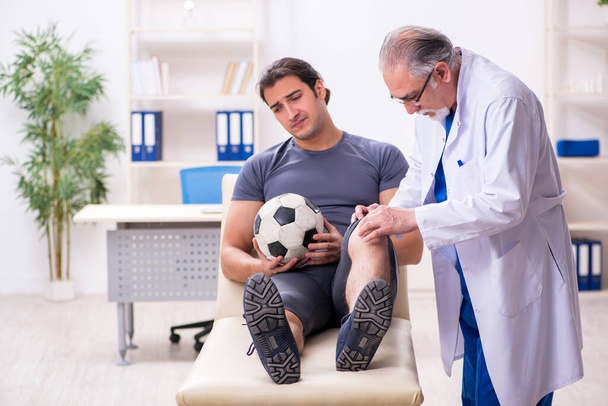 Young injured soccer player visiting old doctor traumatologist - Valokuva, kuva