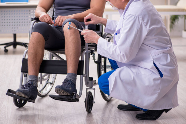 Joven paciente masculino en silla de ruedas visitando al viejo doctor - Foto, Imagen